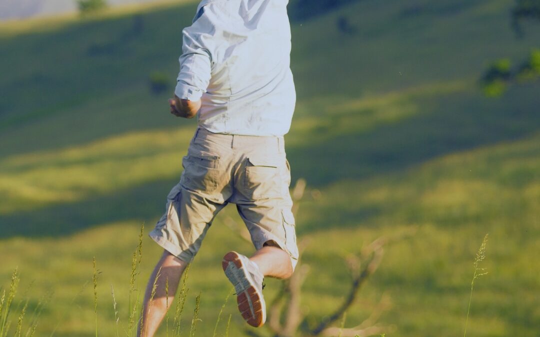 Man jumping and raising hand. Grass in background. Prioritizing mental health.